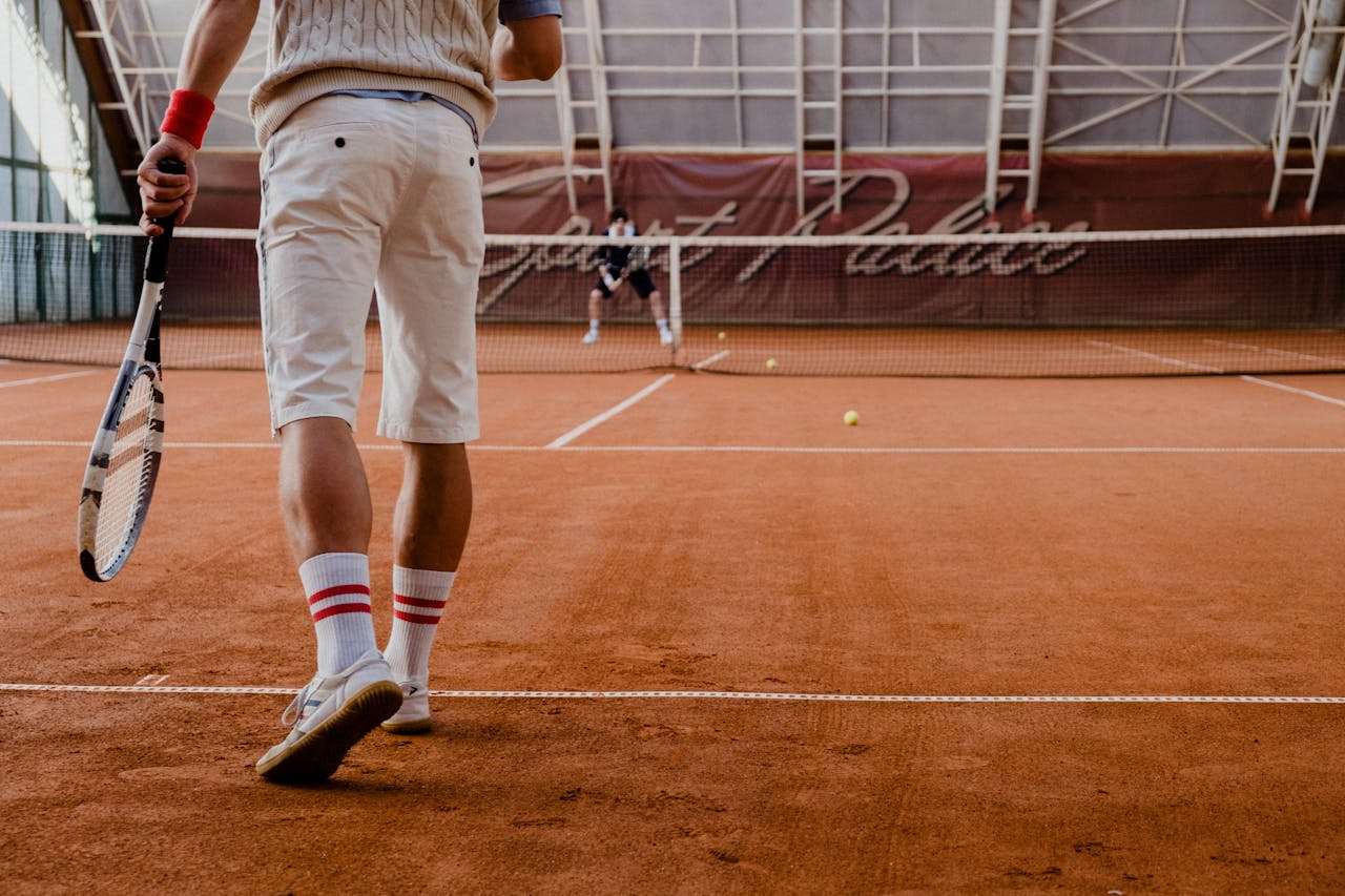 about-img-01 Players competing in a tennis match on an indoor clay court.